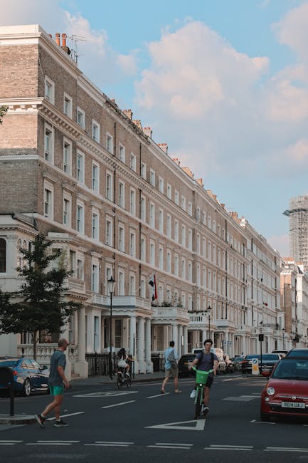 A shot of a historic red brick residential building located on a quiet street in West Kensington, Hammersmith and Fulham. The building features multiple large windows with white frames, some with flow