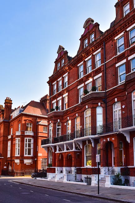 The image shows a large, historic red-brick building with ornate architectural details, including pointed gables, decorative stonework, and tall, arched windows. The front facade features multiple lev